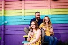 a man and two women sitting on a bench in front of a rainbow colored building