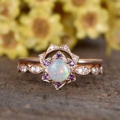 a white opal surrounded by purple and white diamonds sits on a wooden surface with flowers in the background