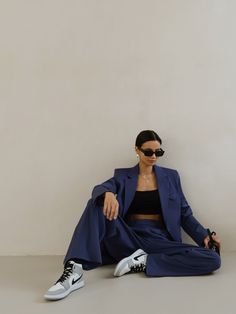 a woman sitting on the ground wearing sunglasses and a blue suit with white sneakers,