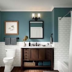 a white toilet sitting next to a bathroom sink under a mirror above a wooden cabinet