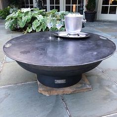 an outdoor table with two wine glasses on it and a potted plant in the background