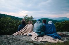 three people sitting on top of a rock looking at the mountains