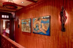 three paintings hang on the wall next to a wooden banister in a room with wood paneling