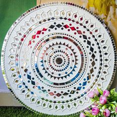 a white plate sitting on top of a green grass covered ground next to flowers and a painting