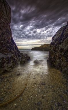 an image of a beach scene with rocks and water under a cloudy sky at night