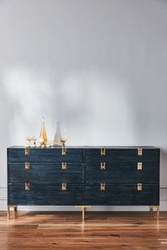 a large blue dresser with gold handles on it in a white walled room next to a wooden floor