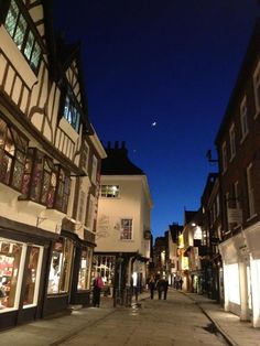 people are walking down the street in front of shops at night time with lights on