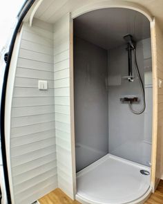 an empty shower stall with wooden flooring and white walls in a home bathroom area