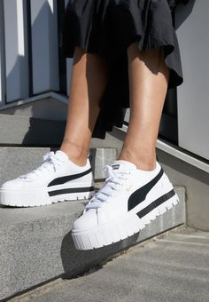 a woman's feet wearing white sneakers and black skirt sitting on concrete steps with her legs crossed