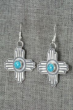 These turquoise and sterling silver New Mexico Zia symbol shaped earrings were made by Navajo silversmith Kevin Billah. The backs are signed KB and stamped sterling.Length: 2 1/4"Width: 1 3/8"Free shipping on all orders! We ship with USPS and always include tracking. All orders ship within a day of payment.Returns are accepted up to 30 days after you receive your order. Just send us a message. Our shop offers cash back or store credit. The item must be returned in new condition. Turquoise Concho Dangle Jewelry, Sterling Silver Turquoise Concho Jewelry, Unique Sterling Silver Concho Jewelry, Traditional Concho Earrings For Gift, Traditional Concho Earrings As Gift, Artisan Turquoise Sterling Silver Earrings, Artisan Turquoise Concho Earrings, Handmade Southwestern Sterling Silver Earrings, Artisan Stamped 925 Earrings