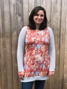 a woman standing in front of a wooden fence wearing an orange and blue floral top