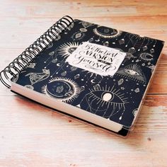 a black and white notebook with the words happy halloween on it sitting on a wooden surface