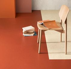 a stack of books sitting on top of a red floor next to a wooden chair