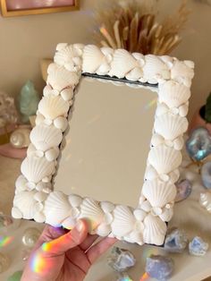 a person holding up a mirror with shells on it