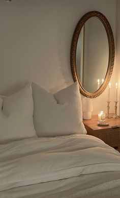 a bed with white sheets and pillows in front of a round mirror