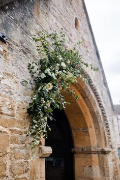 an archway with flowers on it in front of a stone wall and doorway to another building