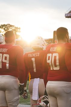 three football players are standing on the sidelines with their helmets up and facing each other