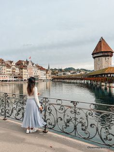 a woman is standing on a bridge looking at the water and buildings in the background