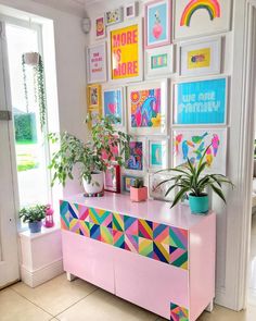 a pink dresser topped with potted plants in front of a wall filled with pictures