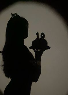 the silhouette of a woman holding a cake in front of a round object with letters on it