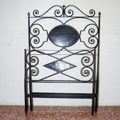 a metal headboard with an iron frame and decorative designs on the top, against a white wall