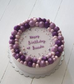 a birthday cake with purple frosting and flowers on it sitting on a white table