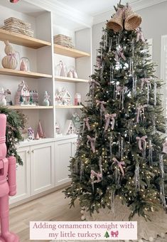 a christmas tree decorated with pink bows and ornaments in a room filled with white shelves