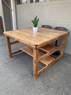 a wooden table sitting on top of a cement floor next to a garage door with a potted plant in it