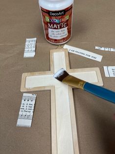 a wooden cross sitting on top of a table next to a paintbrush and glue