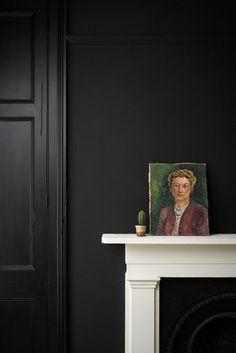 a black room with a white fireplace and painting on the mantle