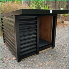 an outdoor storage shed with shutters open on gravel ground in front of trees and bushes