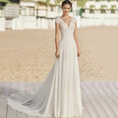 a woman in a white wedding dress standing on a wooden deck at the beach with her back to the camera