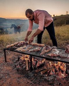 a man grilling steaks on an open fire in the middle of a field