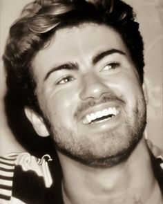 a black and white photo of a man with curly hair smiling at the camera while wearing a striped shirt