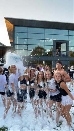 a group of young people standing next to each other in front of a building covered in snow