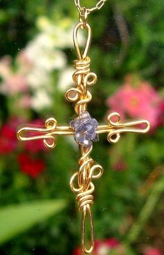 a cross made out of gold wire with a blue bead hanging from it's side