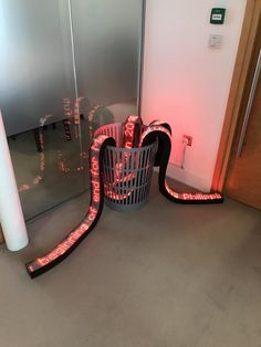 a metal trash can sitting in front of a glass door with red light on it