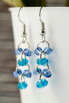 blue glass beads hang from silver earwires on a white cup with a plant in the background