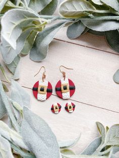 a pair of red and white earrings on top of a wooden table next to eucalyptus leaves