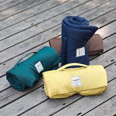 three different colored blankets sitting on top of a wooden floor next to each other, one folded up and the other closed