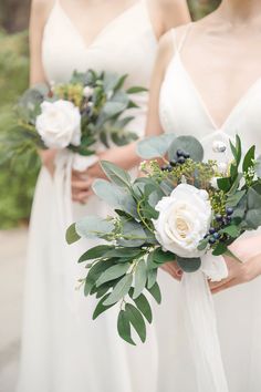 three bridesmaids in white dresses holding bouquets with greenery and flowers on them