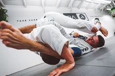 two men in white shirts and blue pants are doing tricks on a black mat with their hands