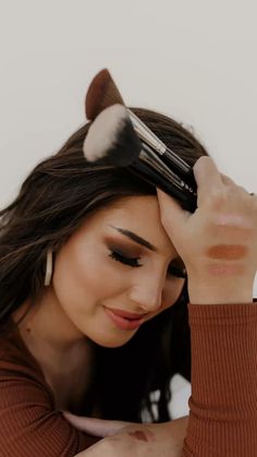 a woman is holding her hair up to her face with the brush in front of her head