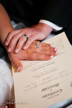 the bride and groom are holding hands on top of a wedding program with rings on their fingers