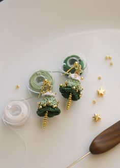 two green earrings sitting on top of a white plate next to spools of thread