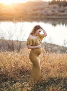 a pregnant woman in a mustard colored dress poses for a photo by a lake at sunset