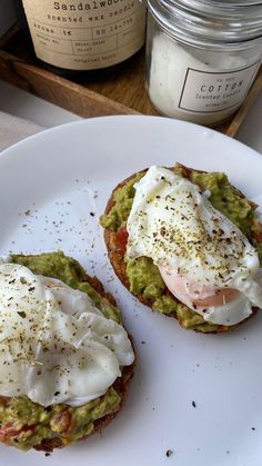 two open faced sandwiches with an egg on top sit on a plate next to a jar of coffee