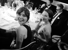 black and white photograph of three women sitting at a dinner table with other people in the background