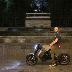 a man standing next to a motorcycle in front of a fountain with lights on it