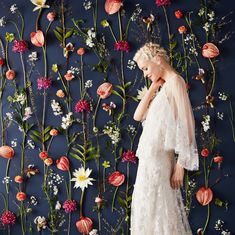 a woman is standing in front of a wall with flowers on it and she has her hands behind her head